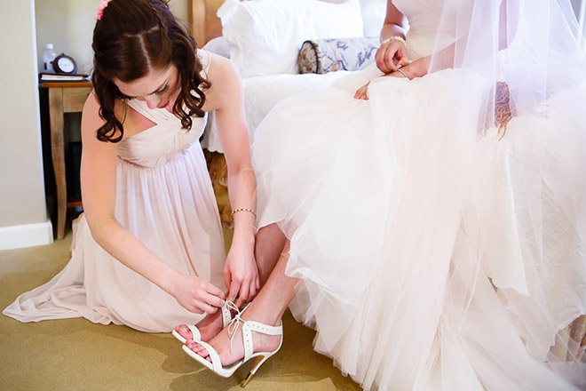 bridesmaid helping bride put her shoes on